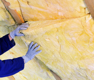 A person wearing blue gloves installs insulation in ceiling